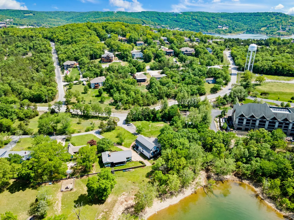 A tranquil lakeside community scene at sunset, showing the lake shore, surrounding homes, water tower, and trees. The view captures the serene atmosphere of the area and suggests possibilities for boating, fishing, and lakeside picnics.