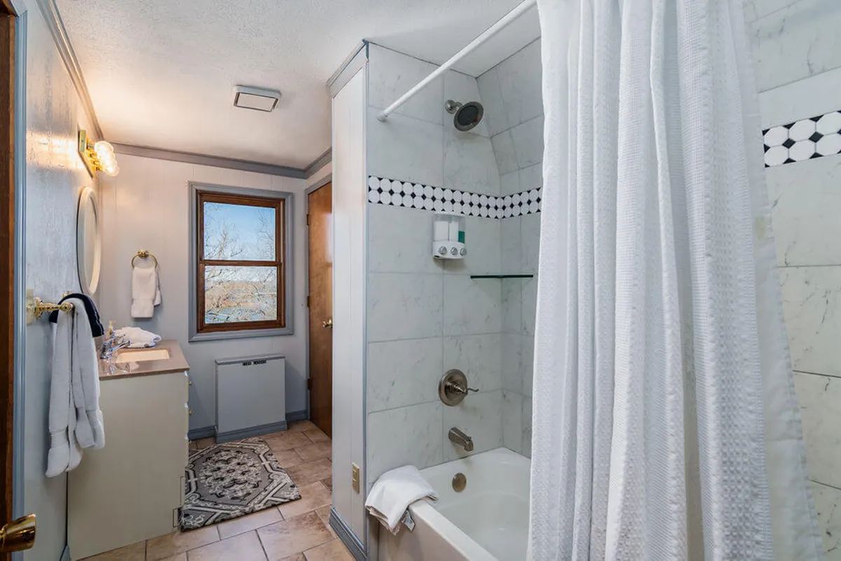 A serene private bathroom with a bright window letting in morning sunlight, a relaxing bathtub, a wide mirror above a vanity, and calming, neutral décor. The space feels airy and fresh, ideal for peaceful morning routines or evening relaxation.