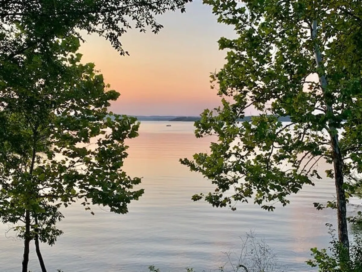 This view features calm water, distant hills, and a colorful sky—capturing the tranquility and beauty of the lakeside setting. It suggests opportunities for fishing, boating, lakeside picnics, and campfires, all under a serene sunset or starlit sky.