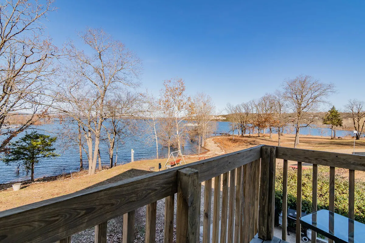 This image captures a tranquil lakeside view with calm water, bare trees, a pathway, and a deck railing. The scene suggests direct access to Table Rock Lake and conveys opportunities for fishing, boating, walking, or simply enjoying the outdoors.