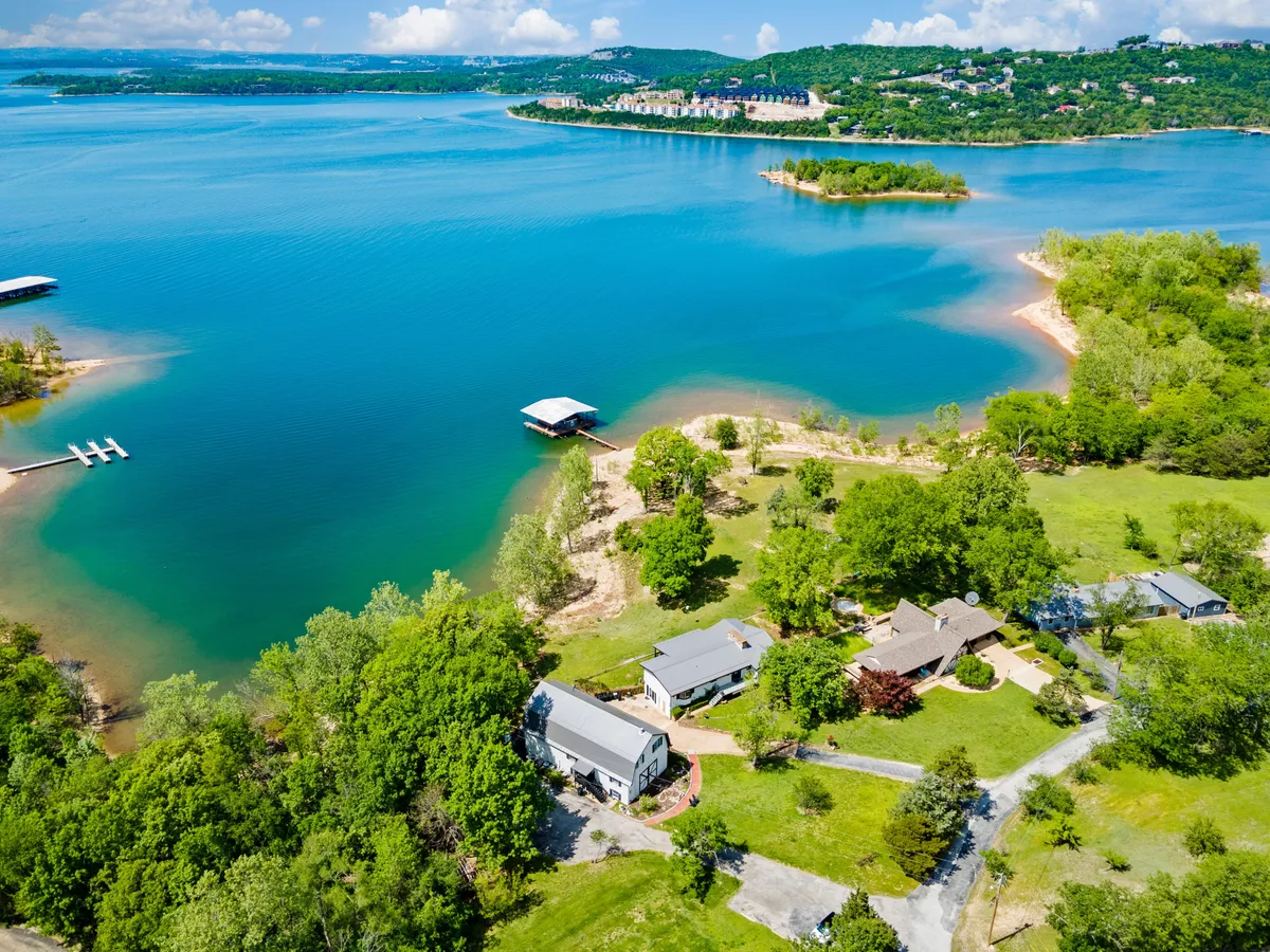 This exterior shot captures the lake, the dock extending out over the water, nearby houses, and lush greenery. It reflects an inviting lakeside setting where guests might fish, launch kayaks, or gather for a barbecue on the lawn.